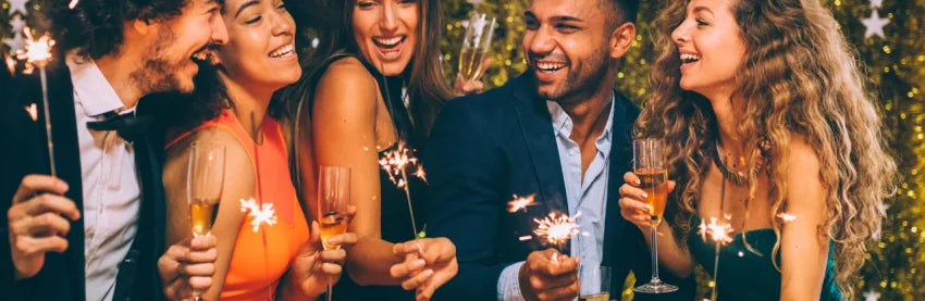 Freunde feiern gemeinsam Silvester mit Getränk und Sprühkerze auf hellem Hintergrund