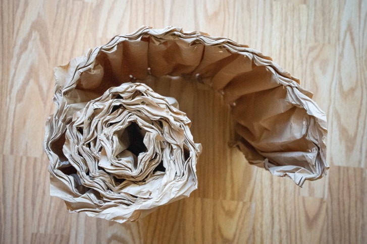 Papierschlauch liegt spiralig aufgerollt auf Holzboden, von oben betrachtet.