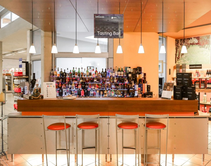 Barhocker stehen vor einer Tasting-Bar mit vielen Alkopflaschen und einem Schild darüber.