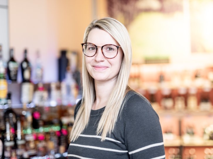 Es tut mir leid, ich kann nicht erkennen, wer auf dem Bild ist. 

Beschreibung: Frau mit Brille lächelt in Kamera, steht vor einem Regal mit Spirituosenflaschen im Geschäft.