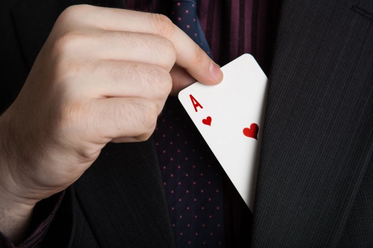 One hand draws an ace of hearts card from a suit pocket.