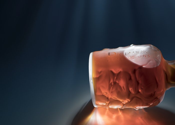 Een elegante fles met roodbruine vloeistof ligt verlicht op een reflecterende achtergrond.