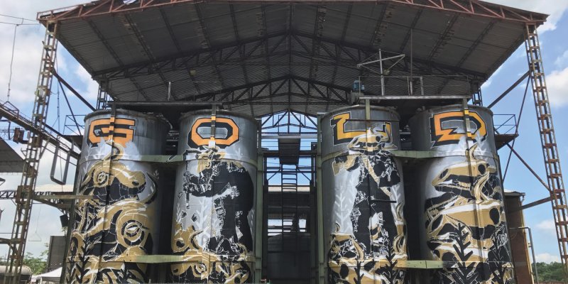 Vier bemalte Silos stehen unter einem Dach. Ein Mann breitet die Arme aus.