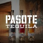 Drie Pasote tequila flessen staan naast elkaar op een houten oppervlak voor een rustieke muur.