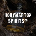 Tussen stukken hout in het bos ligt een jeneverfles met de tekst "Roby Marton Spirits Co.