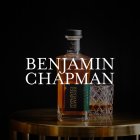 Fles Benjamin Chapman Whiskey staat op een gouden tafel, zwarte achtergrond.