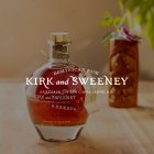 Een Kirk en Sweeney Reserva rumfles staat op een houten tafel naast een decoratief glas.