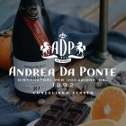 Fles wijn staat naast chocolade en sinaasappels op een houten tafel, tekst "Andrea Da Ponte".