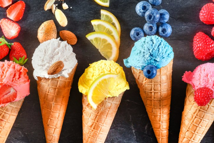 Bunte Eiskugeln in Waffeln, verziert mit Früchten und Schokolade, auf dunklem Hintergrund arrangiert.
