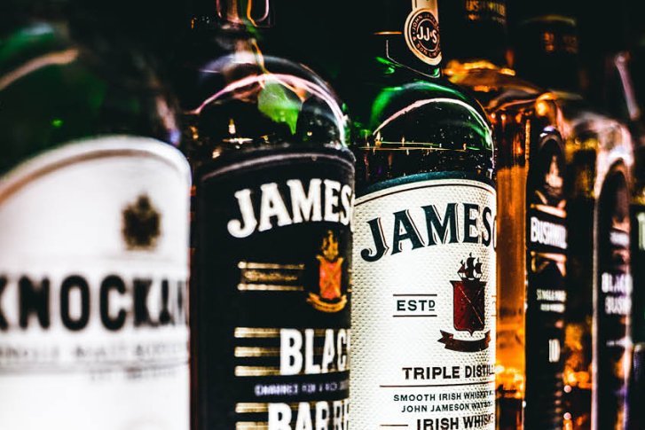 Flaschen Alkohol stehen in einer Reihe, beleuchtet, in einem dunklen Regal.