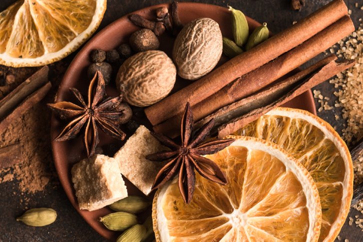 Trockenfrüchte, Gewürze und Zucker liegen arrangiert auf einem dunklen Untergrund.