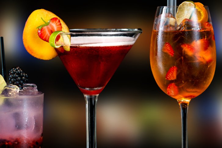 Fünf Cocktails stehen aufgereiht, elegant dekoriert, vor einem unscharfen, festlichen Hintergrund.