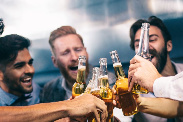 Männer stoßen fröhlich mit Bierflaschen an, in einer geselligen Bar-Umgebung.