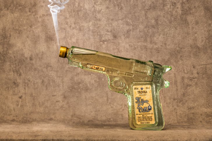 Grüne Glasflasche in Pistolenform steht auf Tisch, Rauch steigt aus dem Flaschenhals auf.