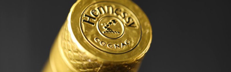 Goldener Flaschenverschluss mit "Hennessy Cognac" Aufschrift, beleuchtet in dunklem Hintergrund.