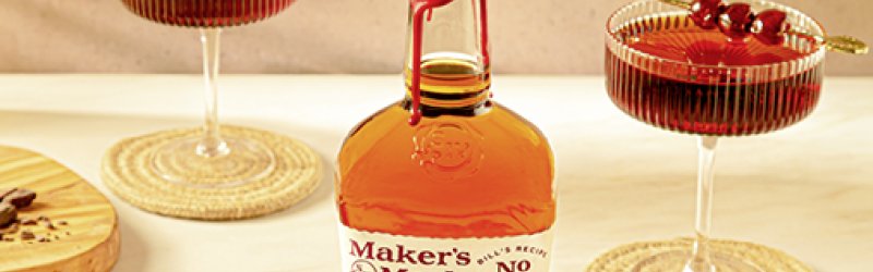 Une bouteille de Maker's Mark est posée sur la table, flanquée de deux verres à cocktail contenant des boissons rouges.