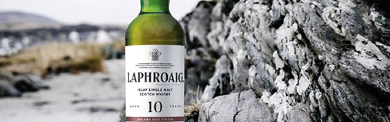 Eine Whiskyflasche steht auf Felsen mit einem gefüllten Glas daneben in natürlicher Umgebung.