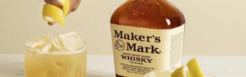 Le citron est pressé dans un verre à whisky, la bouteille de whisky Maker's Mark est posée à côté sur la table.