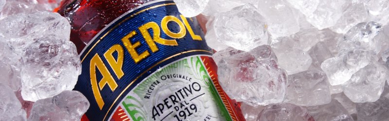 Flasche Aperol liegt in Eiswürfeln, das bunte Etikett mit dem Schriftzug ist sichtbar.