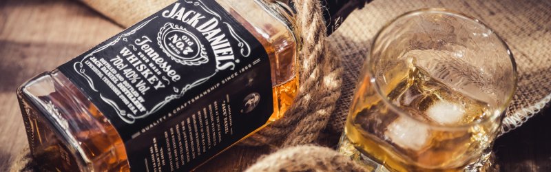 Une bouteille de whisky est posée sur une corde, à côté d'un verre rempli de glaçons sur une table en bois.
