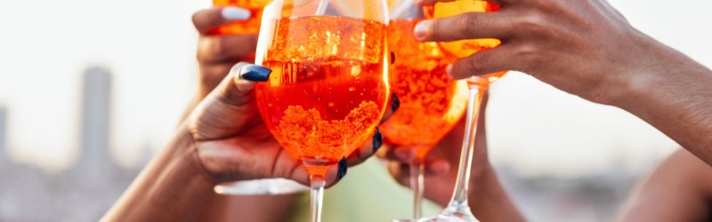 Des verres de boisson orange portent un toast, en plein air avec une skyline floue en arrière-plan.