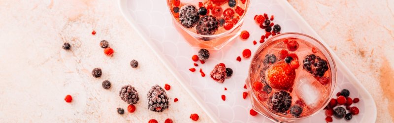 Two glasses of berries and ice cubes stand on a tray, surrounded by scattered berries.