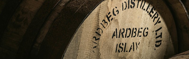Wooden cask labeled "Ardbeg Distillery Ltd" stands in a dark storage environment.
