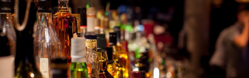 Various bottles stand close together on a bar in a dark environment.