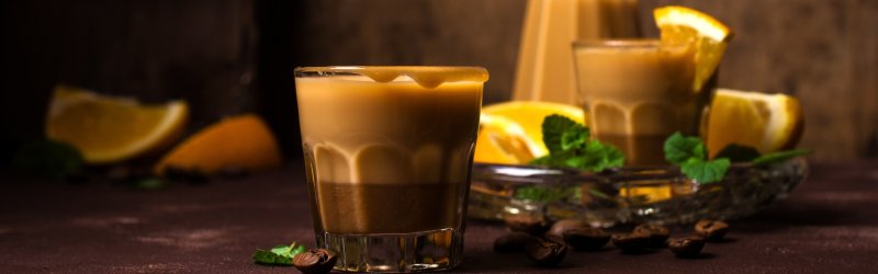 A glass of creamy drink stands on a table, surrounded by oranges and mint.