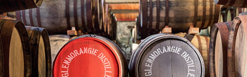 Wooden barrels lying in a warehouse. Two barrels with "THE GLENMORANGIE DISTILLERY" prominently visible.