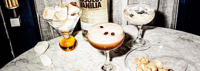 Glasses of cocktails stand on a marble table, surrounded by popcorn and marshmallows.