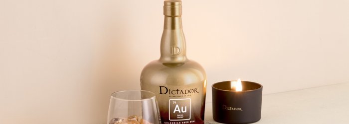 Een rumfles en glas staan naast een brandende kaars op een lichtgekleurd oppervlak.