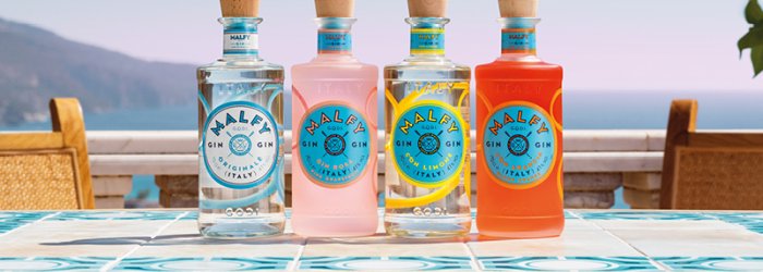 Four colorful bottles of gin stand on a decorative table with a sea view in a sunny setting.