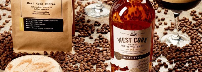 Eine Nahaufnahme in Augenhöhe zeigt eine Vielzahl von Gegenständen, die mit West Cork Distillers in Verbindung stehen, vor einem Hintergrund aus verstreuten Kaffeebohnen in einem warmen Farbton.