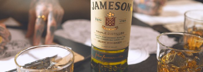 Eine Jameson-Whiskeyflasche steht auf einem Tisch neben gefüllten Gläsern und Unterlagen.