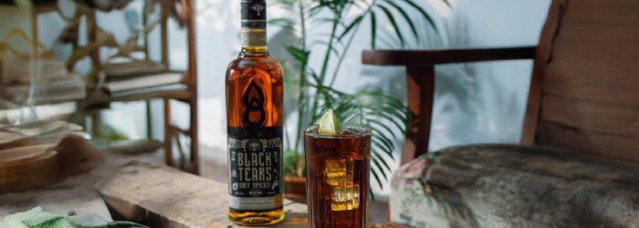 Een fles Black Tears met een zomerse achtergrond zoals een palmboom.