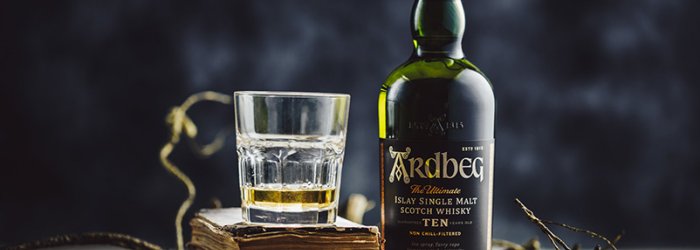 Een whiskyfles en een glas staan op oude boeken, omringd door takken.
