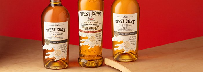 Drei Flaschen The Glenturret Single Malt Scotch stehen auf einer hölzernen Fassdaube vor einem roten Hintergrund in einer horizontalen Aufnahme auf Augenhöhe. Die Flaschen sind so angeordnet, dass eine in der Mitte steht und die anderen links und rec