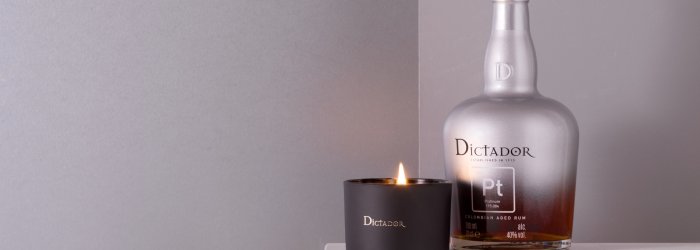 Rumfles naast een brandende kaars op een marmeren oppervlak tegen een grijze achtergrond. Tekst: "Dictador".