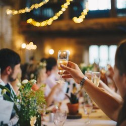 Person holding champagne glass, in festively decorated room, at a convivial dinner with fairy lights.